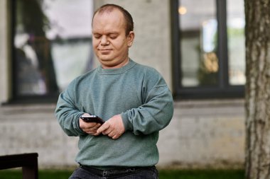 A man with inclusivity in a green sweater checks his phone while walking in a city setting. clipart