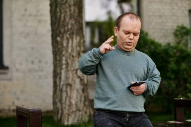 Elinde telefon olan bir adam parkta el kol hareketi yapar ve konuşur..