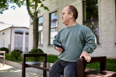 A man with inclusivity sits on a bench, holding a phone, in front of a building. clipart