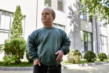 Çevresi yeşilliklerle çevrili bir binanın dışında özgüvenle duran bir adam kapsayıcılığın ruhunu somutlaştırıyor..