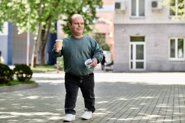 Kapsamlı bir adam elinde kahve fincanı ve belgeyle şehir caddesinde yürüyor..
