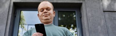 Kapsamlı bir adam şehir merkezindeki bir binanın önünde beklerken telefonunu kontrol ediyor..