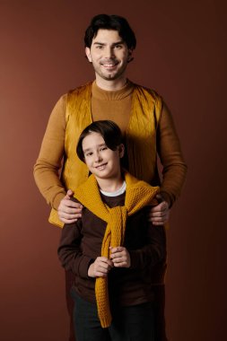 Bir baba ve oğlu birbirlerine uyumlu sarı süveterlerle poz verirler. Gülüşleri sıcak ve sevgi dolu bir bağı yansıtır..