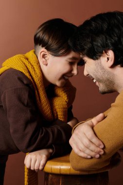 Bir baba ve oğlu birbirlerinin gözlerinin içine bakar, içten bir şekilde gülümserler..