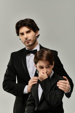 Smokinli bir baba, aynı zamanda smokin giyen ve eli omuzunda olan oğluna sakince güvence verir..