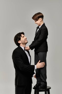 Takım elbiseli bir baba ve oğul, gri bir zemine karşı hassas bir anı paylaşıyorlar..