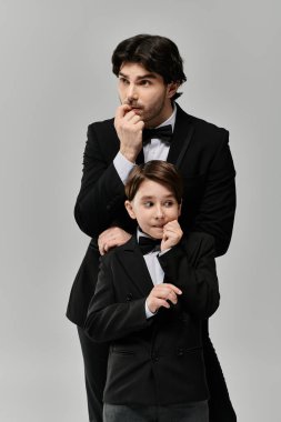 A father and son, both in black suits, stand together with the father gently placing his hand on the sons shoulder. clipart