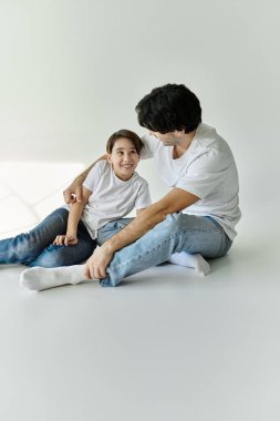 A father and son are sitting on a white floor, smiling and looking at each other. clipart