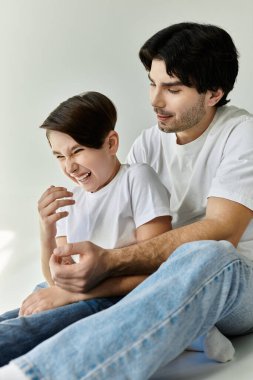 Bir baba ve oğul yerde otururken bir an neşe ve kahkaha paylaşırlar..
