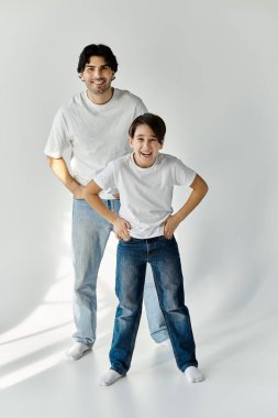 A father and his son are standing in a white room, both smiling and looking at the camera. clipart