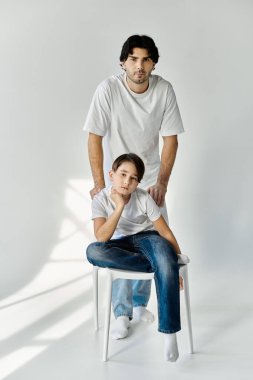Beyaz tişörtlü bir baba ve oğlu beyaz bir stüdyoda fotoğraf çektirmek için poz veriyorlar..