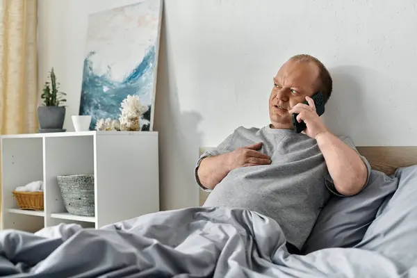 stock image A man with inclusivity sits in bed talking on the phone.