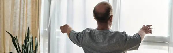 stock image A man with inclusivity stands near a window with his arms outstretched, welcoming the day.