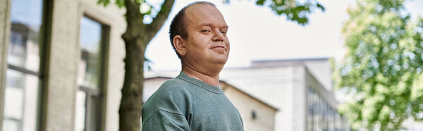 A man with inclusivity stands in front of a building, looking off to the side.