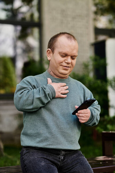 A man with inclusivity sits on a bench in a park, looking at his phone with a smile.