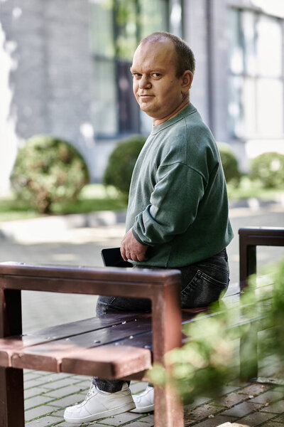 Мужчина с инклюзивностью сидит на скамейке в парке и заботливо смотрит.