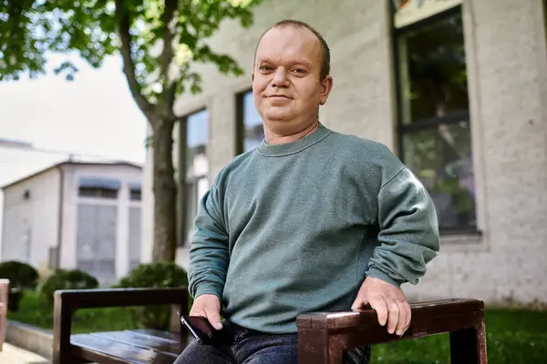 stock image A man with inclusivity sits on a bench outdoors, looking directly at the camera.