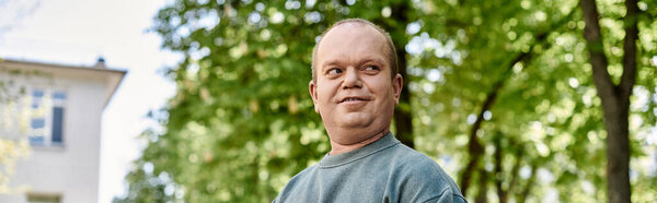 A man with inclusivity smiles warmly as he walks through a lush park on a bright summer day.