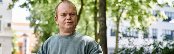 A man with inclusivity stands outside on a sunny day in an urban setting, looking directly at the camera.