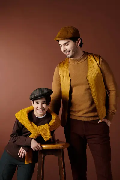 stock image A father and son stand together in a studio setting, both wearing warm brown and yellow clothing. They are smiling and appear to be enjoying each others company.