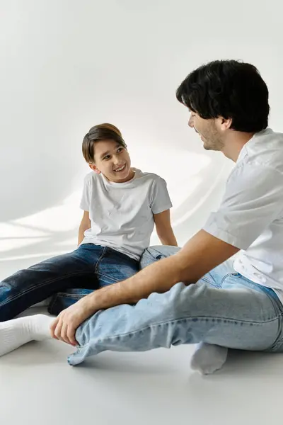 stock image A father and son share a playful moment, sitting on a white floor and laughing together.