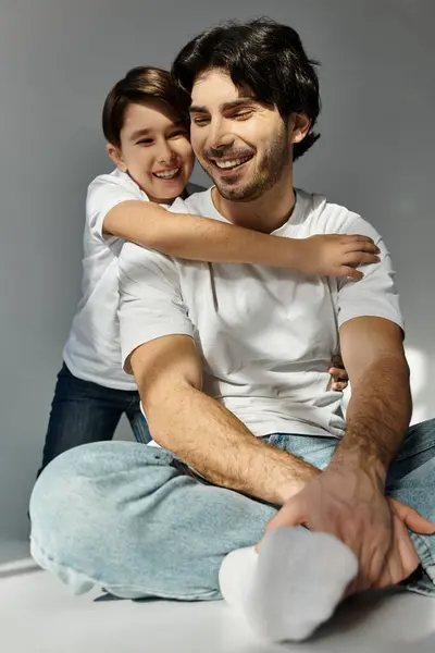 stock image A father and his son sit together, the son embracing his dad from behind, both laughing joyfully.