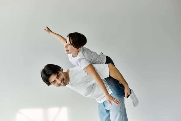 Отец катает сына на спине в закрытом помещении, оба улыбаются.
