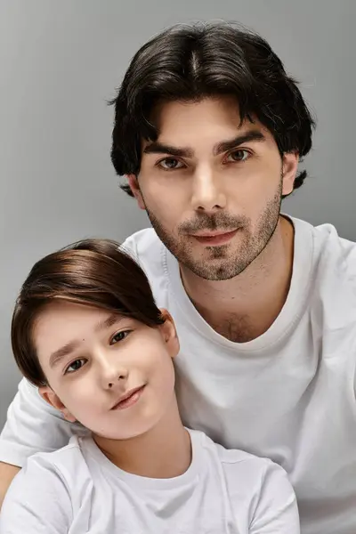 stock image A father and son in white shirts look at the camera with a loving expression.