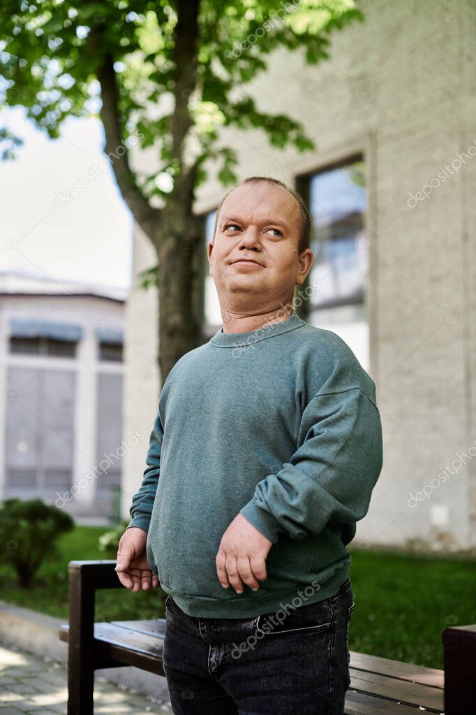 A man with inclusivity in a blue sweatshirt stands outside on a sunny day.