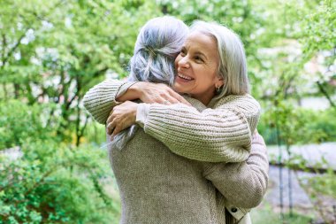 Hırka giyen orta yaşlı bir lezbiyen çift park ortamında birbirlerine sarılıyorlar..