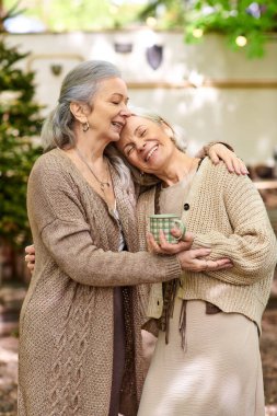 Orta yaşlı ve aşık iki kadın, kamp minibüslerinin yanındaki yeşil bir ormanda hassas bir anı paylaşıyorlar..