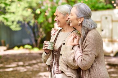 İki orta yaşlı kadın kamp gezisinde kahve içerken birlikte gülüyorlar..