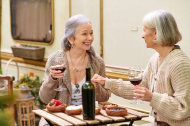 Minibüslerinin yanındaki ormanda kamp yaparken iki orta yaşlı kadın gülüyor ve bir şişe şarabı paylaşıyor..