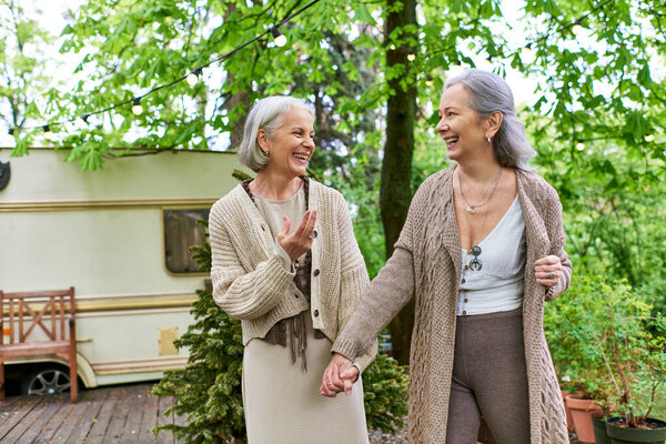 A lesbian couple enjoys a carefree stroll through a verdant forest during a camping trip.