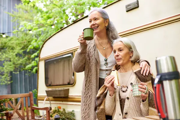 stock image A lesbian couple enjoys a relaxing morning with coffee and sandwiches while camping in a lush green forest.