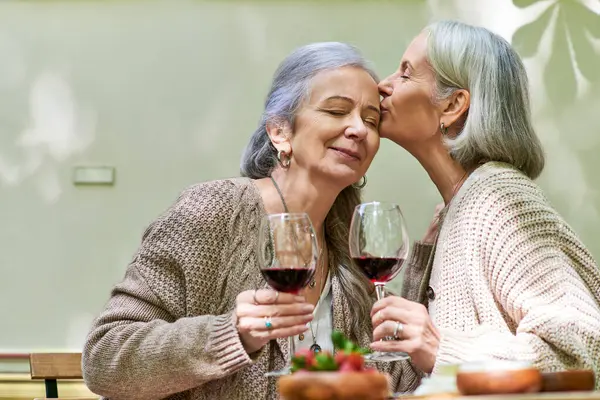 stock image Two women share a romantic moment while enjoying wine in a forest setting.