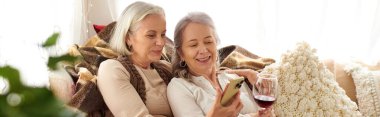 Two women relax in a camper van, one holding a glass of wine while the other uses a phone. clipart