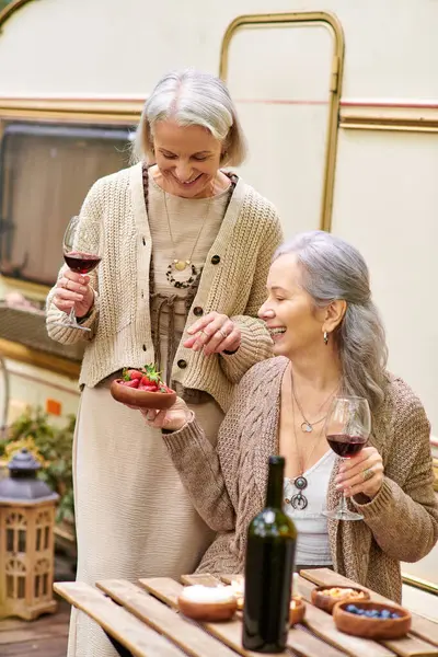 stock image Two middle-aged women enjoy a glass of wine and dessert while camping in a green forest.