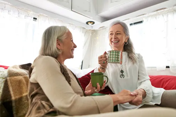 stock image Two women, a lesbian couple, relax in a camping van, enjoying coffee and conversation.