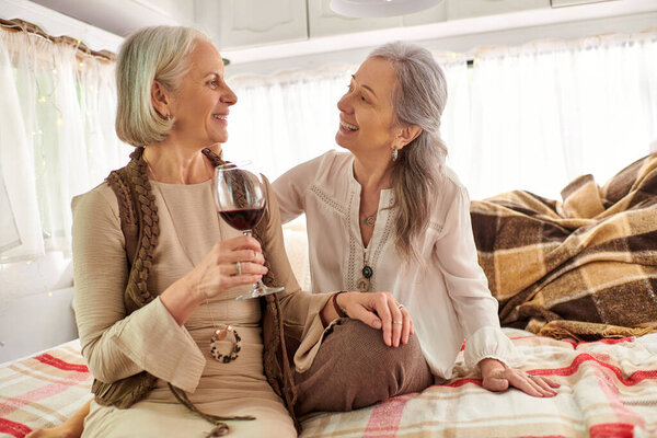 Two middle-aged women enjoy a glass of wine in their cozy camper van during a road trip.