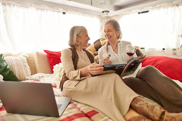 Пара лесбиянок отдыхает в фургоне, выпивает бокал вина и читает журнал.