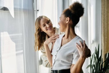 Two women, a diverse lesbian couple, smile at each other while spending time together at home. clipart