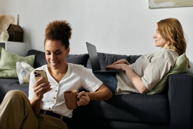 Lezbiyen bir çift evde dinleniyor, biri telefon kullanıyor ve diğeri de dizüstü bilgisayarla çalışıyor..
