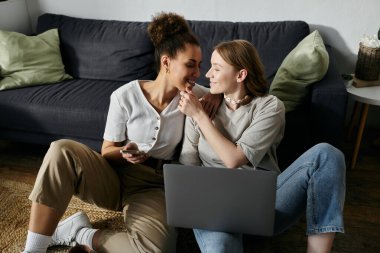 Gündelik giysiler içindeki iki kadın evde dinlenirken hassas bir anı paylaşıyorlar..