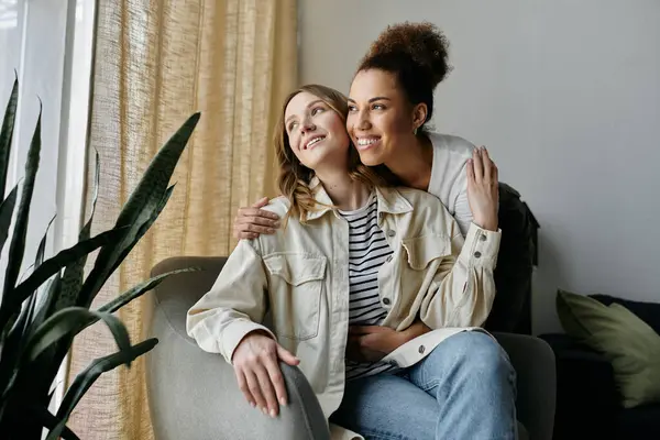 stock image Two women, a diverse lesbian couple, sit together on a couch at home, enjoying a moment of intimacy and affection.