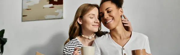 stock image Two women are cuddling in their home, enjoying a cup of coffee together.