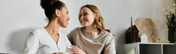 Two women, dressed casually, sit and converse at home, sharing a warm moment together.