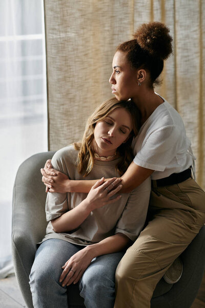 A lesbian couple embraces each other while relaxing at home.