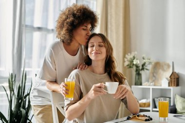 Lezbiyen bir çift evde sıcak bir kahvaltı yaparken, bir kadın diğerini alnından öpüyor..