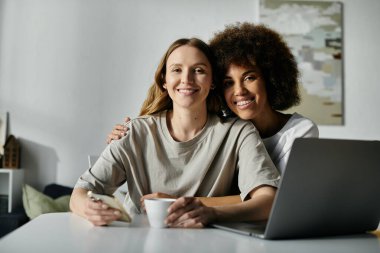 İki kadın, günlük giysiler içinde, sıcak bir öğleden sonra evde eğlenirken kameraya sıcak bir şekilde gülümsüyor..